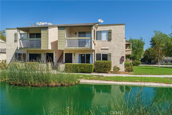 Front view of a two-story building with balconies and a small pond in front.