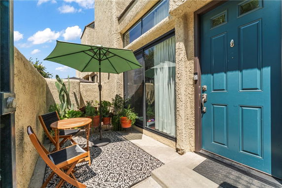 Front view of a house entrance with a blue door, large window, and small patio area with chairs and plants.