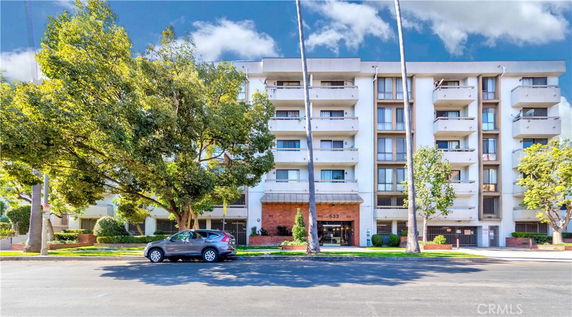 Front view of a multi-story apartment building with balconies and trees in front.