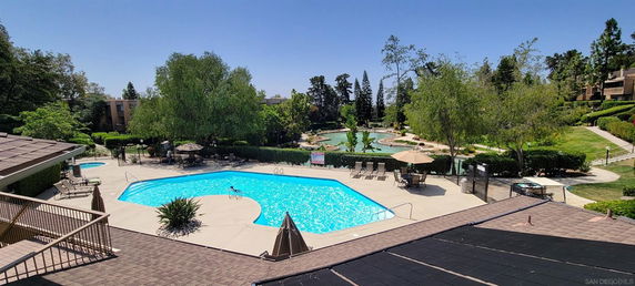 Outdoor swimming pool area surrounded by trees and greenery with a large swimming pool and lounging chairs.