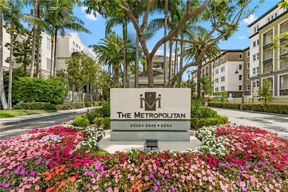 Front view of a multi-story apartment complex with a prominent sign and landscaped surroundings.