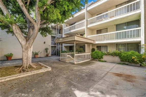 Front view of a multi-story apartment building with balconies and a tree in the courtyard.
