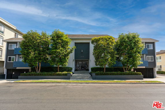 Front view of a multi-story apartment building with trees and a central entrance.