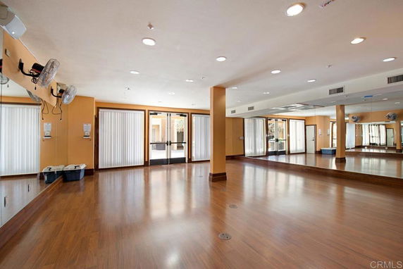 Spacious indoor area with wooden flooring, mirrors, and ceiling fans.