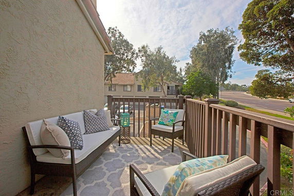 Balcony view with outdoor seating area overlooking trees and residential street.