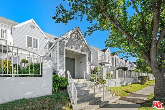 Front view of a white multi-story residential building with entrance steps and surrounding fence.