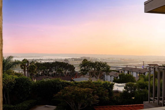 Panoramic view of a residential area with trees and distant landscape at sunset.