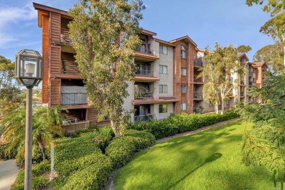 Front view of a multi-story apartment building with balconies and trees nearby.