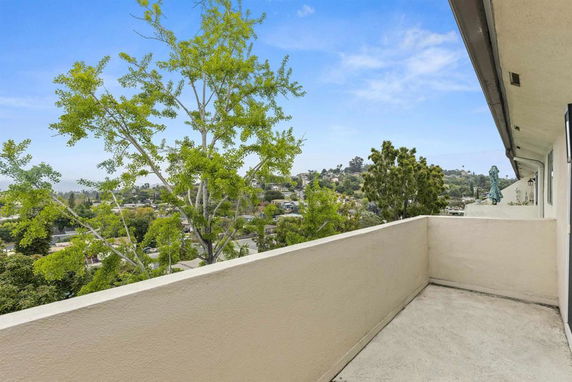 Outdoor view from a building balcony overlooking a residential area with trees and hills in the background.