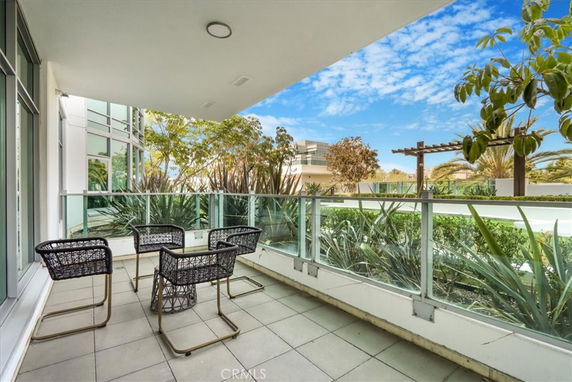 Balcony view with outdoor seating and glass railing, overlooking greenery and nearby buildings.