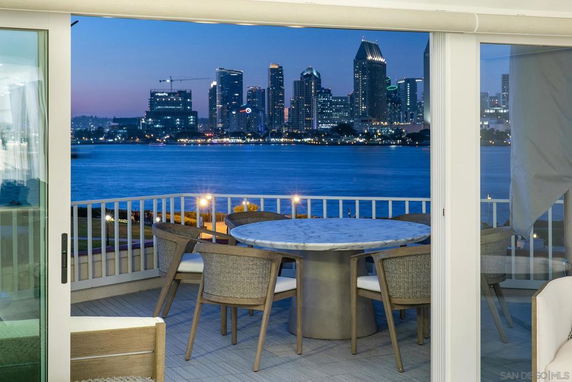 View of a city skyline across a body of water from a balcony with a table and chairs.