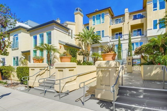 Front view of a multi-story residential building with balconies and landscaped entrance.