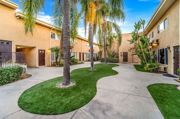 Courtyard view between residential buildings with palm trees and pathways.