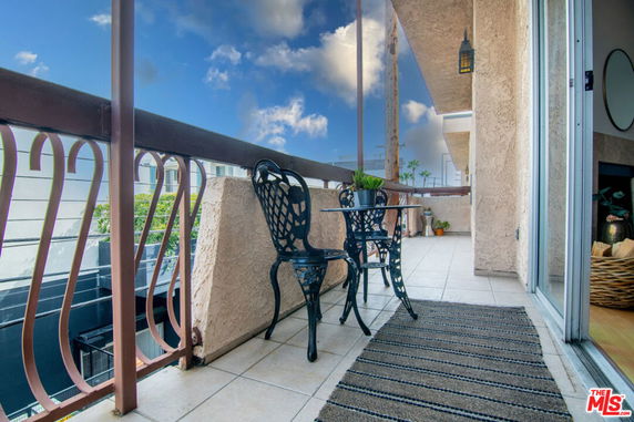 Balcony with metal chairs and table, offering a view of the surrounding structures under a blue sky.