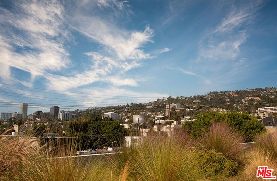 Panoramic view of a cityscape with hills and buildings under a blue sky with clouds.