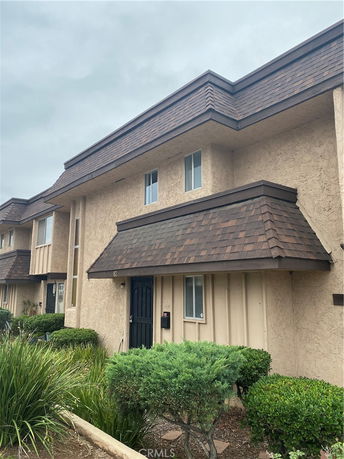 Front view of a two-story house with brown shingled roof and beige stucco walls.