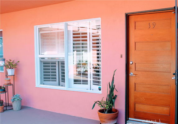 Front view of a house with a wooden door and a window, painted in light pink.
