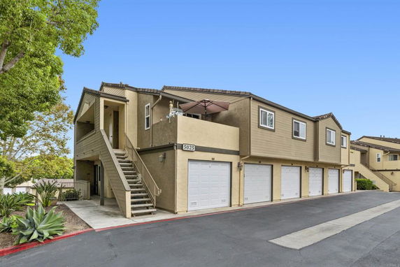 Front view of a multi-unit building with garages on the ground level and an external staircase leading to the upper floor.