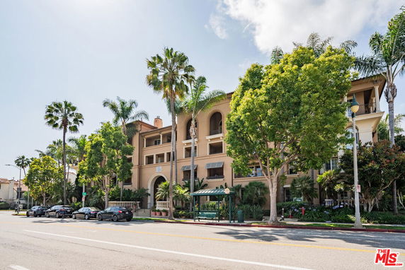 Front view of a multi-story building with balconies and surrounded by palm trees.