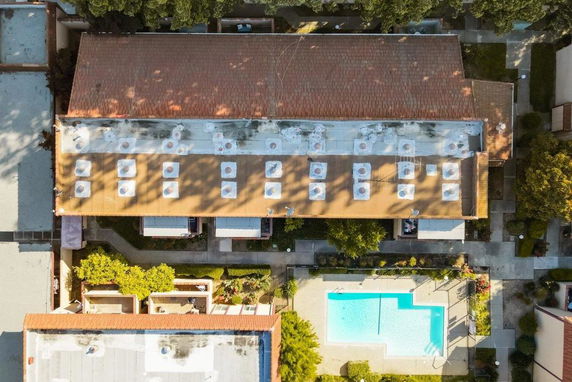 Aerial view of a building with a flat rooftop featuring skylights and adjacent swimming pool.