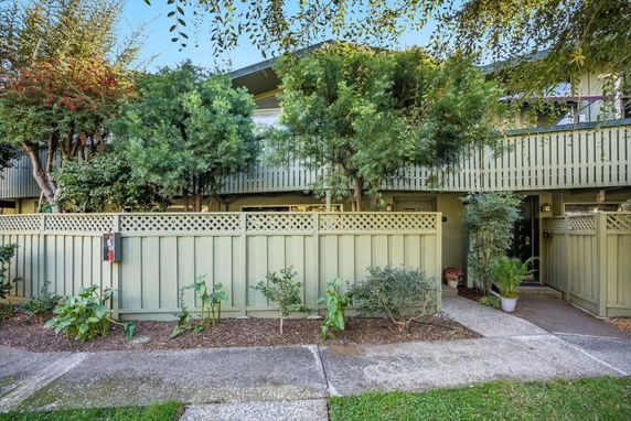 Front view of a two-story residential building with a fence and greenery.