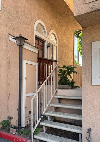 Front entrance of a house with steps leading to a wooden door, accompanied by arched windows.