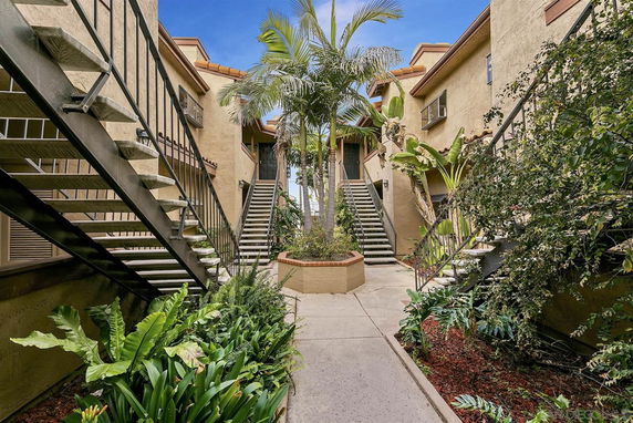 Front view of a multi-story apartment building with exterior staircases and landscaped garden area.