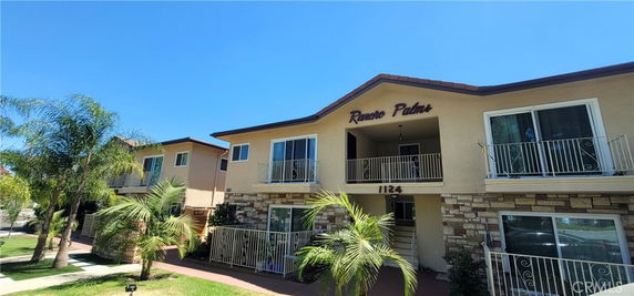 Front view of a two-story apartment building with balconies and palm trees.