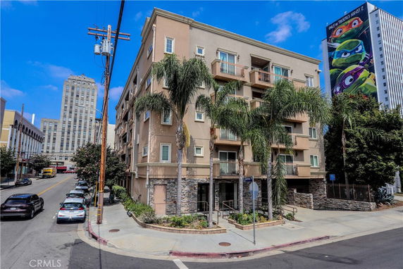 Front view of a multi-story apartment building with balconies and palm trees.