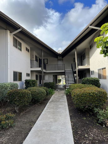 Front view of an apartment building with a central walkway leading to the entrance and external staircases.
