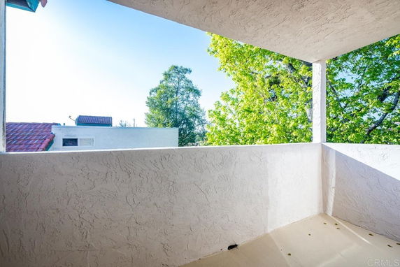 View from a balcony with a plastered wall and trees in the background.