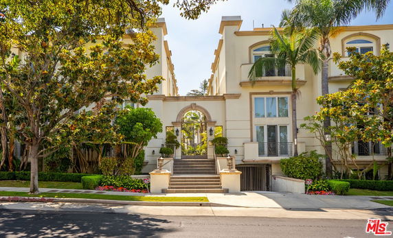 Front view of a multi-story residential building with arched entrance and landscaped surroundings.