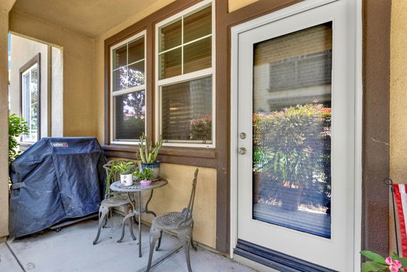 Outdoor patio area with a small table, chairs, and a barbecue grill near a glass door.
