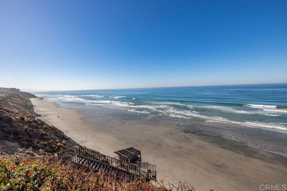 Wide angle view of a beach and ocean with a staircase leading down from the cliff.