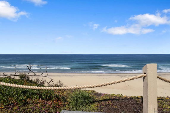 Wide angle view of an ocean and beach from a fenced area with plants.