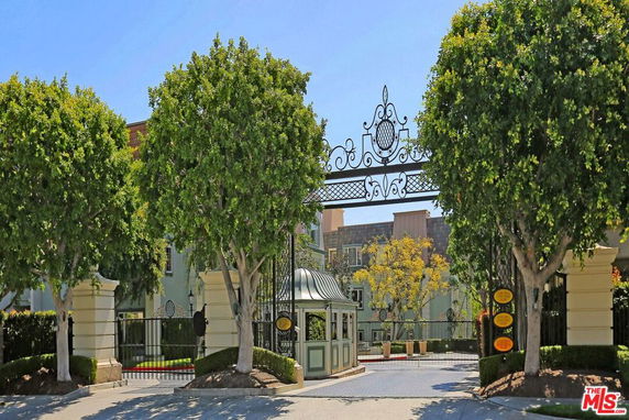 Front view of a gated entrance with ornate ironwork and a security booth.