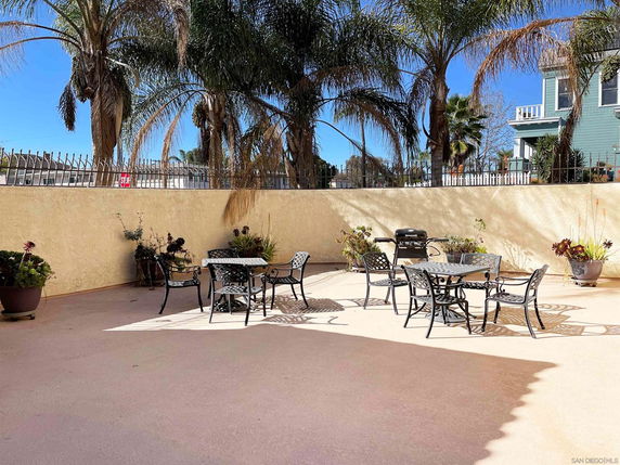 Outdoor patio area with metal tables and chairs, surrounded by a high wall and palm trees.