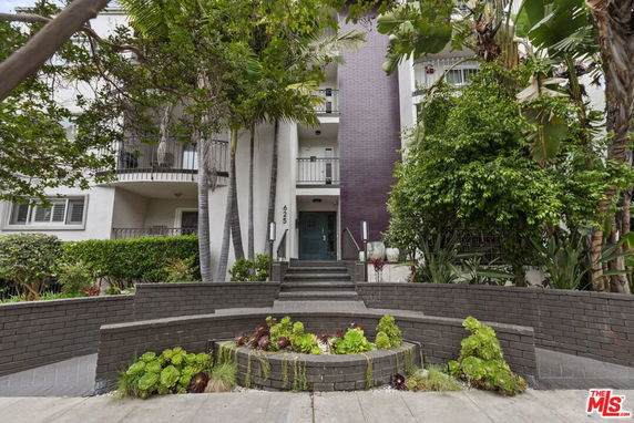 Front view of a multi-story building entrance with stairs and greenery.
