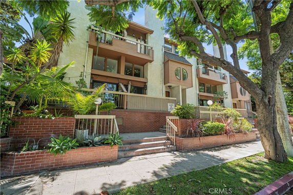 Front view of a multi-story residential building with balconies and landscaped entrance.