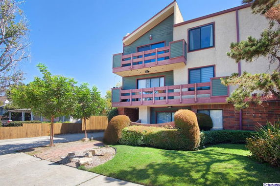 Front view of a multi-story residential building with balconies and landscaped greenery.