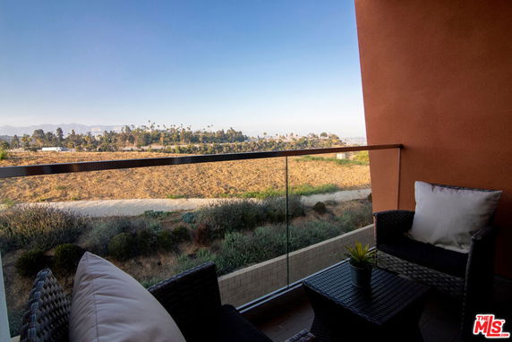 Panoramic view from a balcony with seating, overlooking a natural landscape.