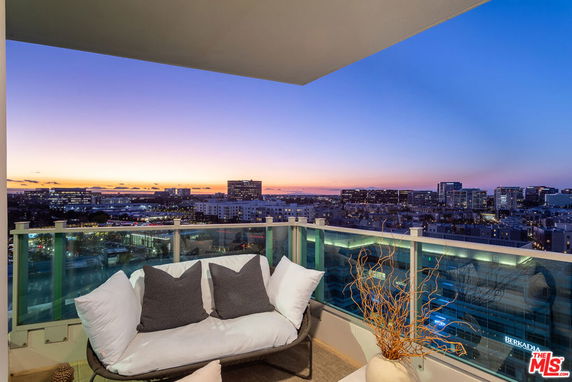 Wide angle view of cityscape from a high-rise balcony with glass railing and outdoor seating.
