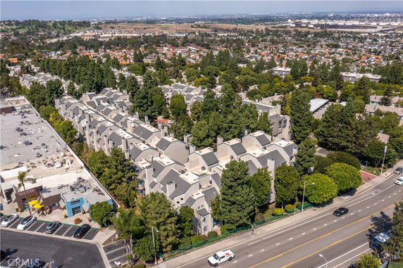 Aerial view of a residential neighborhood with clustered houses and trees, roads and commercial buildings visible.