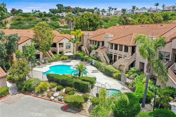 Elevated view of a residential complex with a central swimming pool surrounded by lush greenery and buildings with tiled roofs.