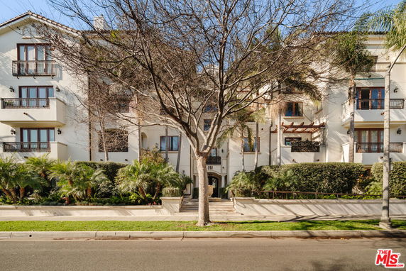 Front view of a multi-story residential building with balconies and a landscaped entrance.