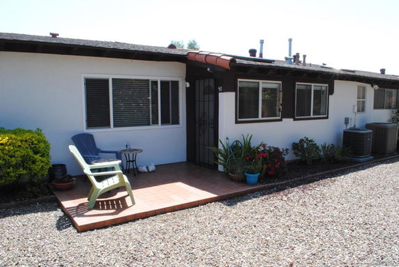 Front view of a single-story house with a small patio and chairs.