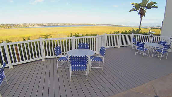 Outdoor patio area with blue and white chairs overlooking a wide view of grassland and a body of water in the background.