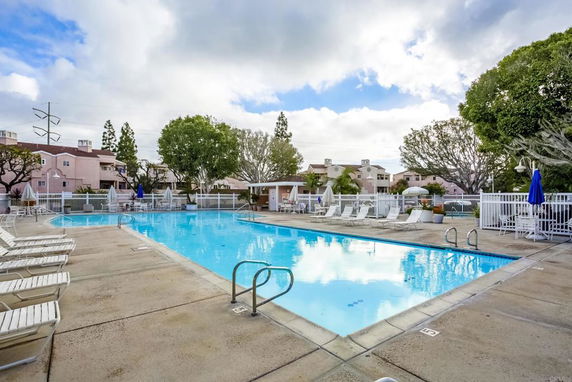 Outdoor swimming pool area with surrounding lounge chairs and buildings.