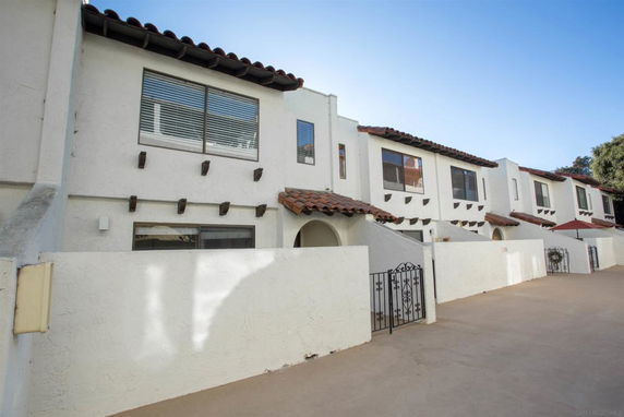 Front view of a row of two-story townhouses with white stucco walls and tiled roofs.