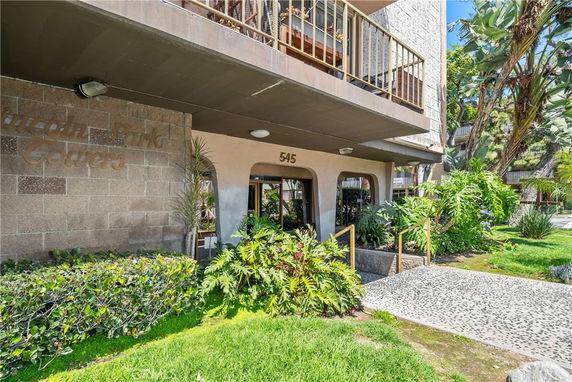 Front view of a building with a balcony and entrance, surrounded by plants.